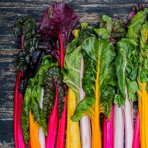 A pile of colorful swiss chard on a wooden counter. Foods such as spinach, avocado, kale, and parsley are high in vitamin E.