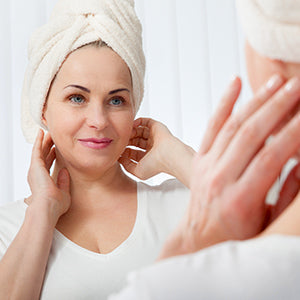 A woman with a towel on her head, looking at herself in the mirror.