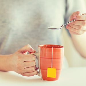 A person is holding a teacup. Aspartame and sucralose are two dangerous artificial sweeteners.