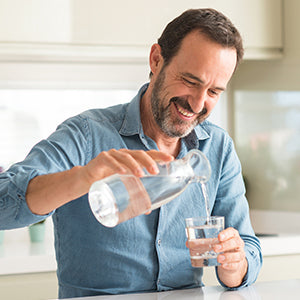 A man pouring water from a jug to a cup in a kitchen setting.