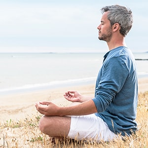 A man meditating on the beach.