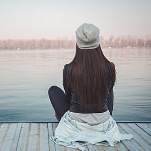 A woman coping with Chronic Fatigue Syndrome by meditating by the lake.