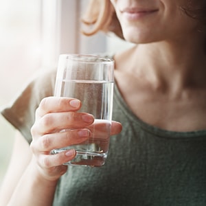 A woman drinking water, which is a natural home remedy for UTIs.