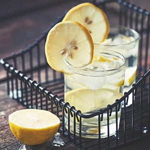 Two glasses of lemon water sitting on a table. Adding lemon water to your daily routine can help you detoxify your body.