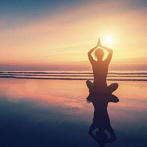 A woman is meditating by the beach. It’s always good to look for signs of high blood pressure on the regular.