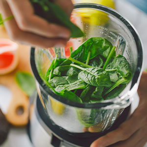 A woman blending a smoothie with spinach and fresh fruits.