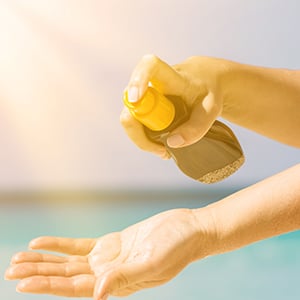 A person spraying sunscreen. Sunscreen contains a number of chemical ingredients that may actually be harmful to your health.