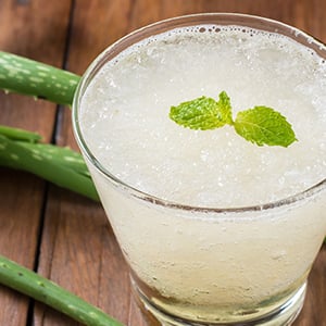 A glass of aloe vera juice with an aloe leaf laying next to it. Aloe vera offers many nutrients and properties that aid digestion.