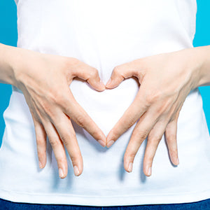 Woman's hands in shape of a heart over her belly.