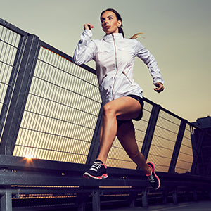 A woman running along a metallic rail with at sunrise.